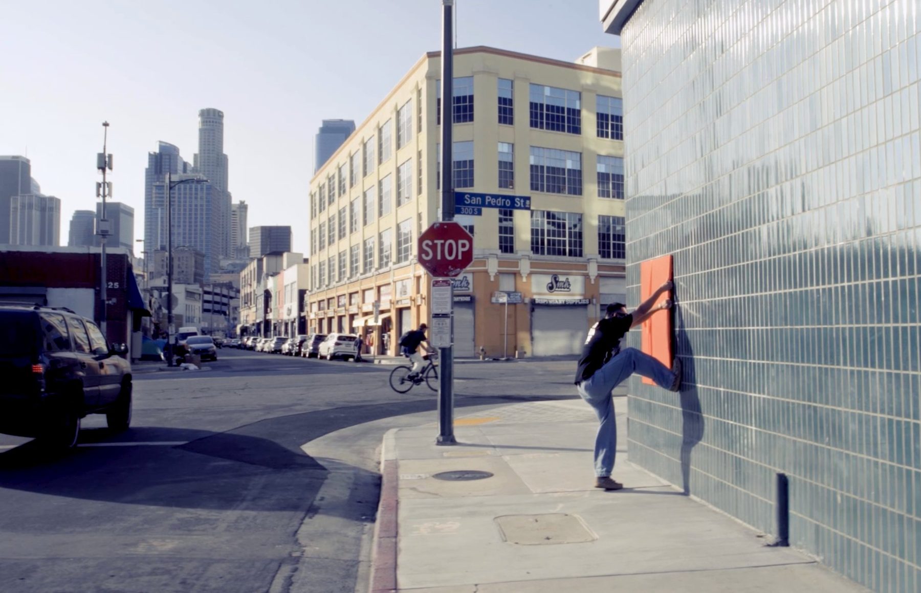 Matt Adam removing an orange-wrapped Unwrap and Steal canvas from a downtown Los Angeles wall on San Pedro Street